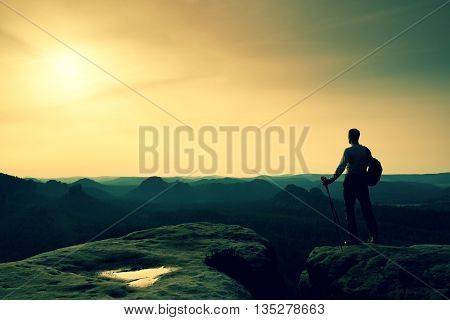 Tourist On Cliff Edge With Pole In Hand And Backpack
