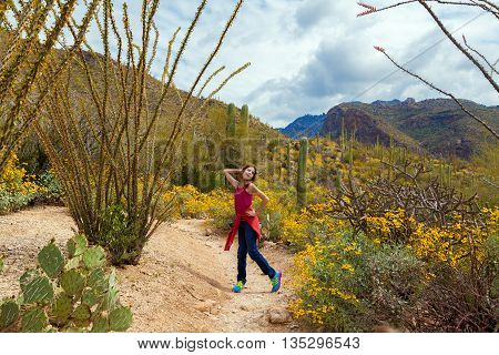 A silly tween girl poses in the Arizona desert on a cloudy day amidst saguaros ocotillos and brittle brush.