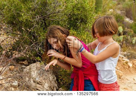 Typical sisters play fighting while laughing. One is wearing a set of play handcuffs as a bracelet. They are in the Arizona desert.