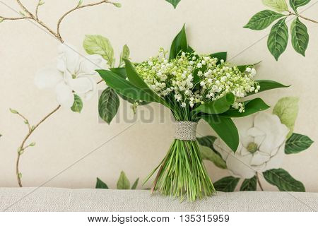Small bouquet of Lily of the valley flowers standing on decorative fabric with floral background in the back. Flower decor idea. Flower design.