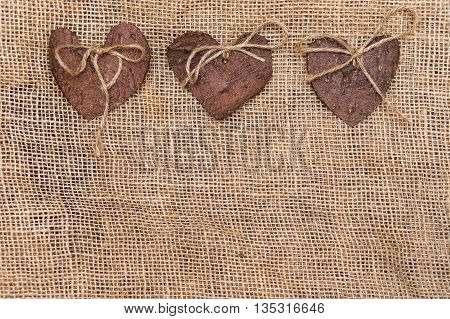 Three (3) decorative hearts made from tree bark on sackcloth, positioned in the middle of the photo. Hearts decorated with eco twine. Eco decor. St. Valentines greeting card idea. Handmade design.