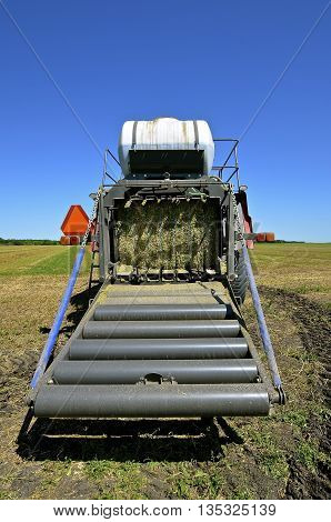 The back of a modern square hay baler where the bale travels down the rollers to meet earth.
