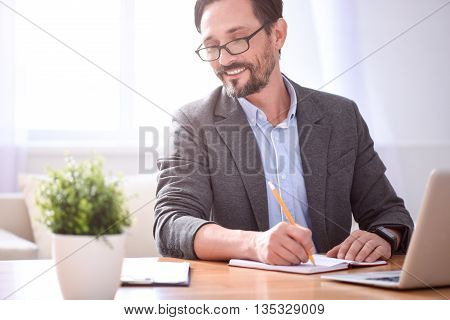 Feeling confident. Contented middle aged man with glasses writing in his notebook and looking at the papers