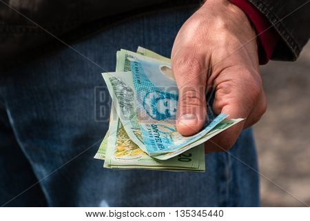 man hand holding New Zealand dollar banknotes