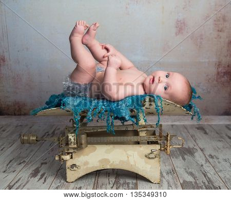 cute little baby with legs up lying on child scales on wooden floor