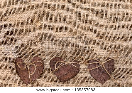 Three (3) decorative hearts made from tree bark on sackcloth, positioned under the middle of the photo. Hearts decorated with eco twine. Eco decor. St. Valentines greeting card idea. Handmade design.