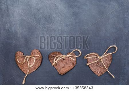 Three (3) decorative hearts made from tree bark on chalkboard, positioned under the middle of the photo. Hearts decorated with eco twine. Eco decor. St. Valentines greeting card idea. Handmade design.
