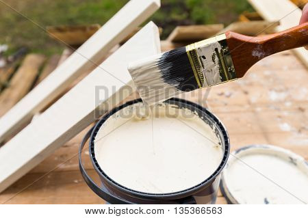 Holding painting brush over the jar with the white paint. Painting timber boards outside with the white paint or white coloured emulsion using 2 inches painting brush.