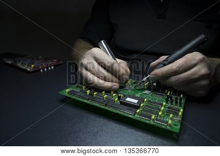Man hands repairing computer motherboard on the black wooden workbench