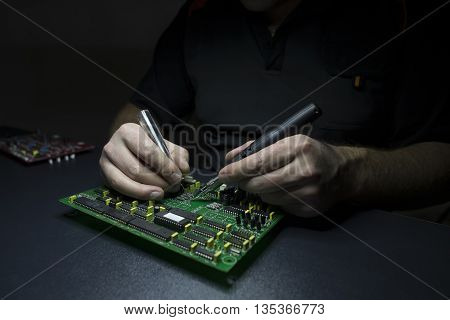 Male hands repairing computer motherboard on the black wooden workbench