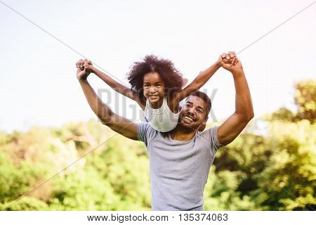 Child flying on father shoulders while held piggyback