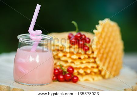 Belgian waffles with fresh berries on cutting board on background of green bokeh. grapefruit juice. pink cocktail with a straw.
