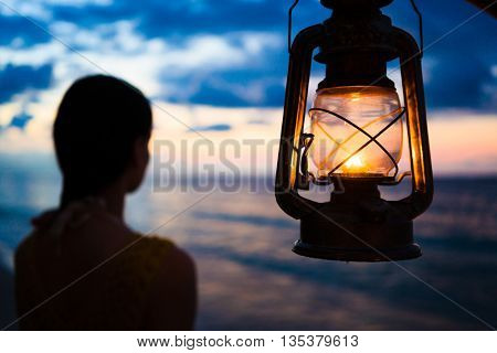 Woman in lantern shine looking to sea at sunset 