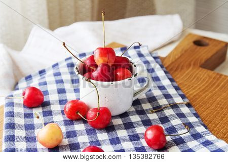 Composition of cup and berries. Cherries is the reason of the longevity . White retro cup and berries on a checkered napkin on the table. Retro cup and berries on a wooden cutting board
