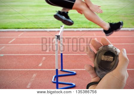 Composite image of coach is holding a stopwatch against selfassured male athlete jumping above hedge during a race
