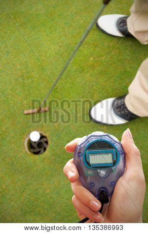 Close up of woman is holding a stopwatch on a white background against golfer putting golf ball in the hole