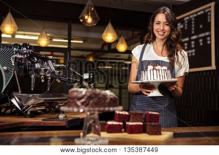 Smiling barista holding plate with cake at coffee shop