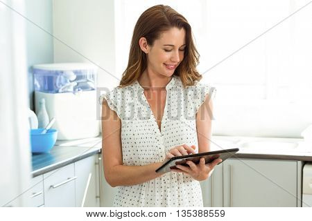 Happy young woman using digital tablet in kitchen