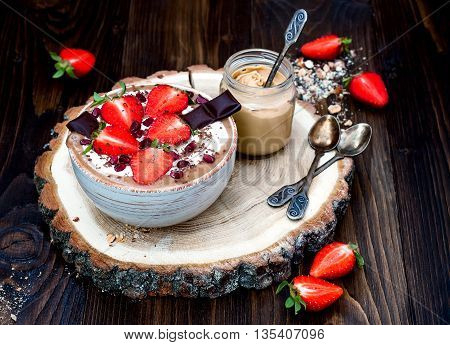Chocolate almond butter maca smoothie bowl topped with sliced strawberries chopped chocolate and pomegranate seeds.