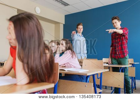 education, bullying, conflict, social relations and people concept - students teasing and judging girl classmate behind her back at school