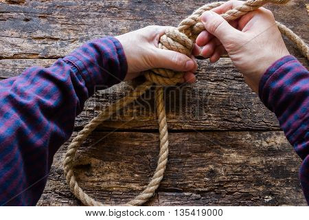 man tying a slipknot on a wooden background