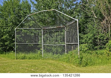 An old baseball backstop sets by itself along a tree line
