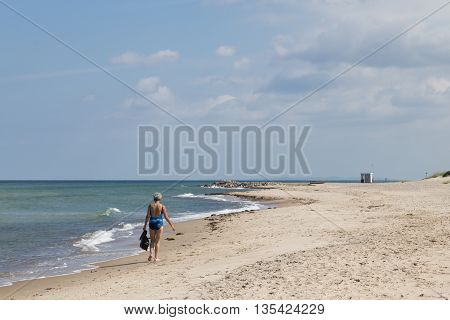 Tisvilde, Denmark - June 20, 2016: An elderly lady walking on Tisvilde beach.