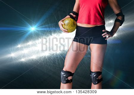 Female athlete with elbow pad holding handball against spotlights