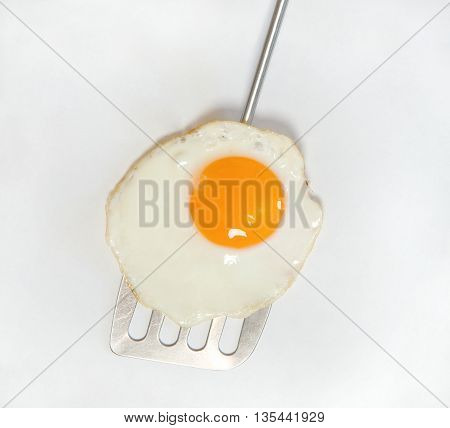 Close up of fried egg on metal spatula isolated on white background.