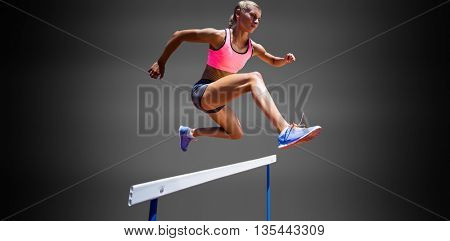 Sporty woman jumping a hurdle against black background