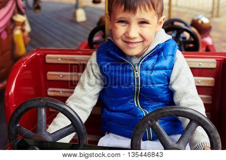 Little boy is sitting in a toy car in amusement park and smiling