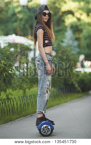 Feet of girl in jeans riding electric mini hover board scooter outdoors in park. Ecological city transportation on battery power.