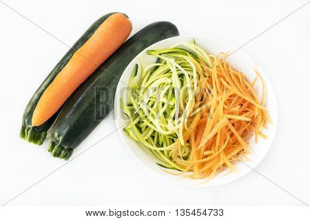 Two zucchini courgettes and carrot with some spiralized in white bowl on white background