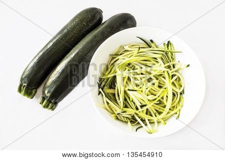 Two zucchini or courgettes with some spiralized in a white bowl on white background