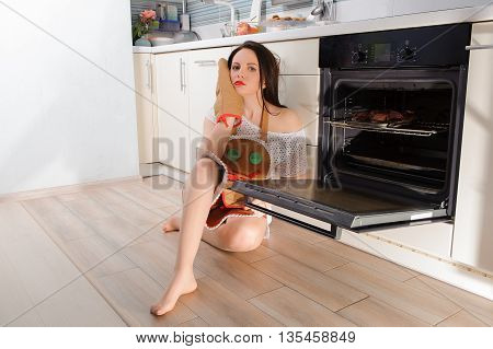 Bored sad young woman sitting next to open oven
