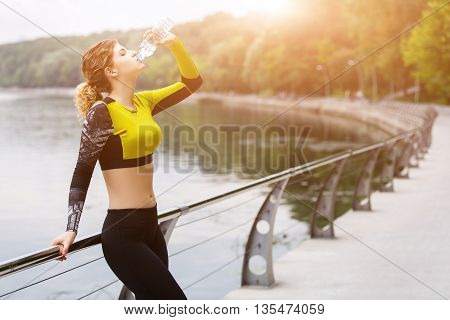 Caucasian woman in sportswear drinking water after sport. Image with lensflare
