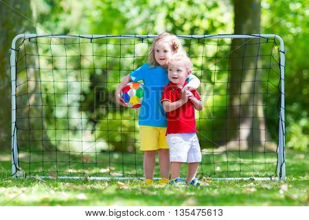 Two happy children playing European football outdoors in school yard. Kids play soccer. Active sport for preschool child. Ball game for young kid team. Boy and girl score a goal in football match.