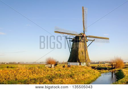 Old thatched windmill in a Dutch polder. The mill was built in 1700. It's a sunny day in winter. A thin layer of ice is on the water.