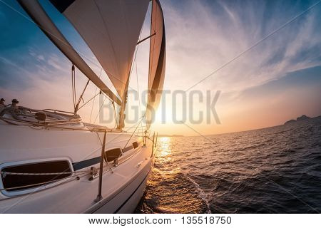 Sail boat with set up sails gliding in open sea at sunset