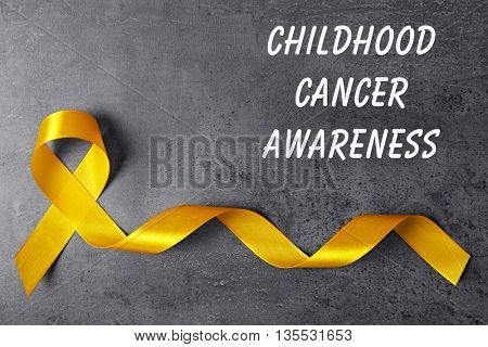 Yellow ribbon and text Childhood Cancer Awareness on grey textured background
