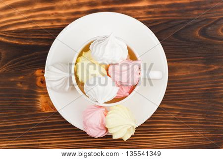 White cup with light pink and white meringues on the wooden background with blank copy space area for text or slogan