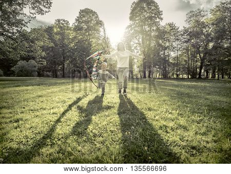 Runnings little boy and mother flies with them kite in the park under sunligt.