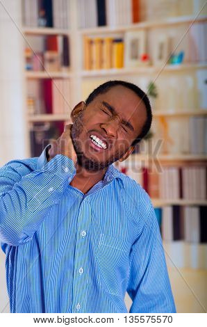 Man suffering a strong pain in his neck, unhappy gace with his hand on his neck