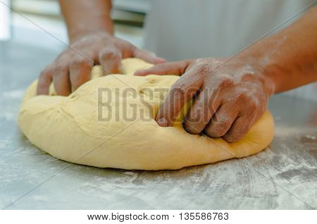 Bakers hands working and kneading large bread dough on metal surface with flour spread out.