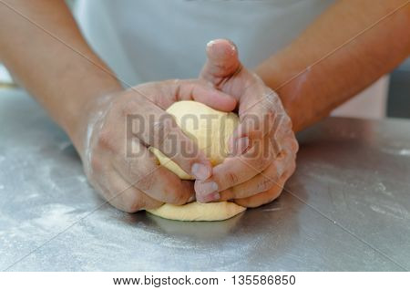 Bakers hands working and kneading bread dough on metal surface.