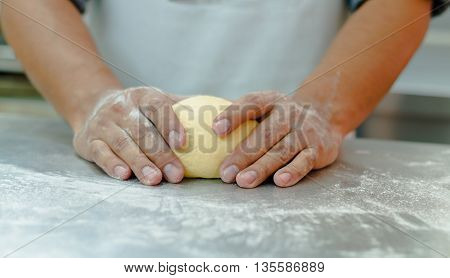 Bakers hands working and kneading bread dough on metal surface.
