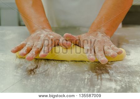 Hands of baker working, kneading and rolling bread dough, shaping into loaf before cooking.