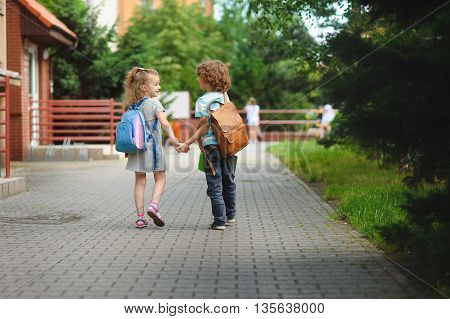 Back to school. Two young students go to school hand in hand. They about something briskly talk. Behind the back of everyone satchel.