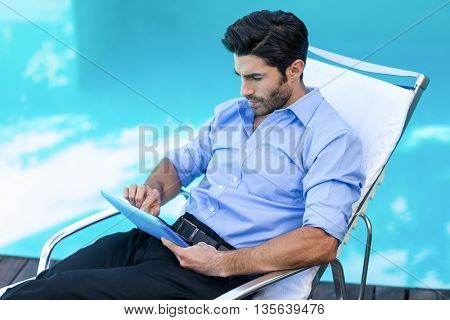 Smart man relaxing on sun lounger and using a digital tablet near the pool