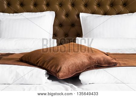 Brown cushion lying on a throw rug over a white duvet on a stylish double bed with upholstered brown headboard close up view